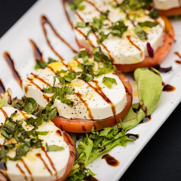 Caprese salad with sliced mozzarella, tomatoes, basil, and balsamic glaze on a white plate.