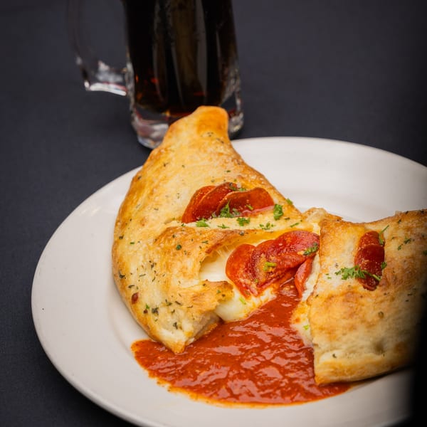 A pepperoni calzone from I Love NY Pizza, cut open with melted cheese and sauce, next to a drink.