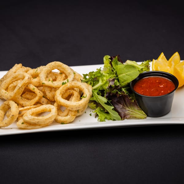 Fried calamari rings with a side salad, marinara sauce, and lemon wedges on a white plate.