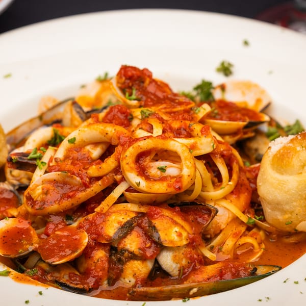 Close-up of linguine pasta with calamari, mussels, clams, and red sauce, served with a bread roll.