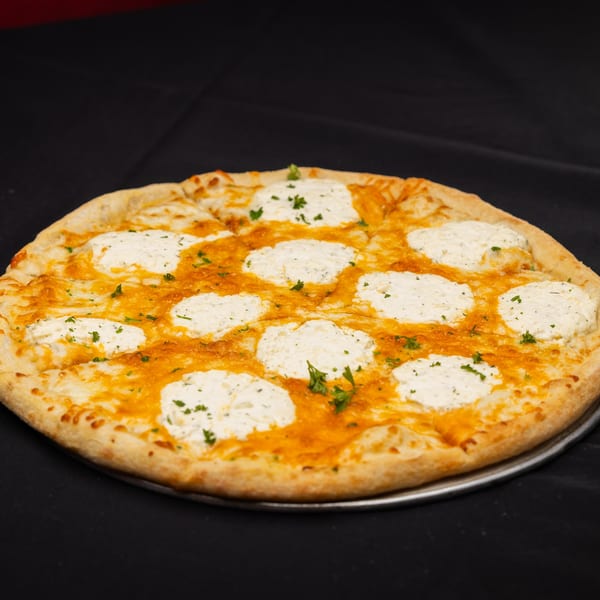 A whole I Love NY Pizza white pizza with dollops of ricotta cheese and parsley on a black background.