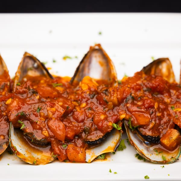 Mussels in a rich red tomato sauce with herbs, served on a white rectangular plate.